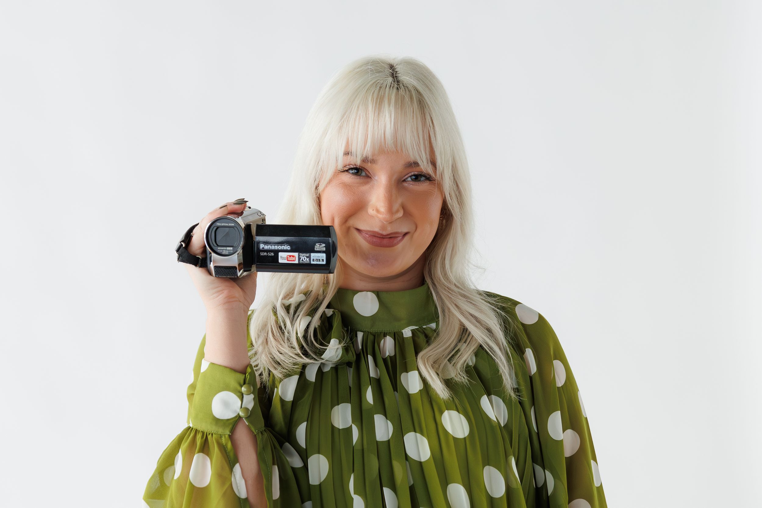 Person in green polka dot sweater holding a vintage camcorder and making silly expressions in a photo collage.