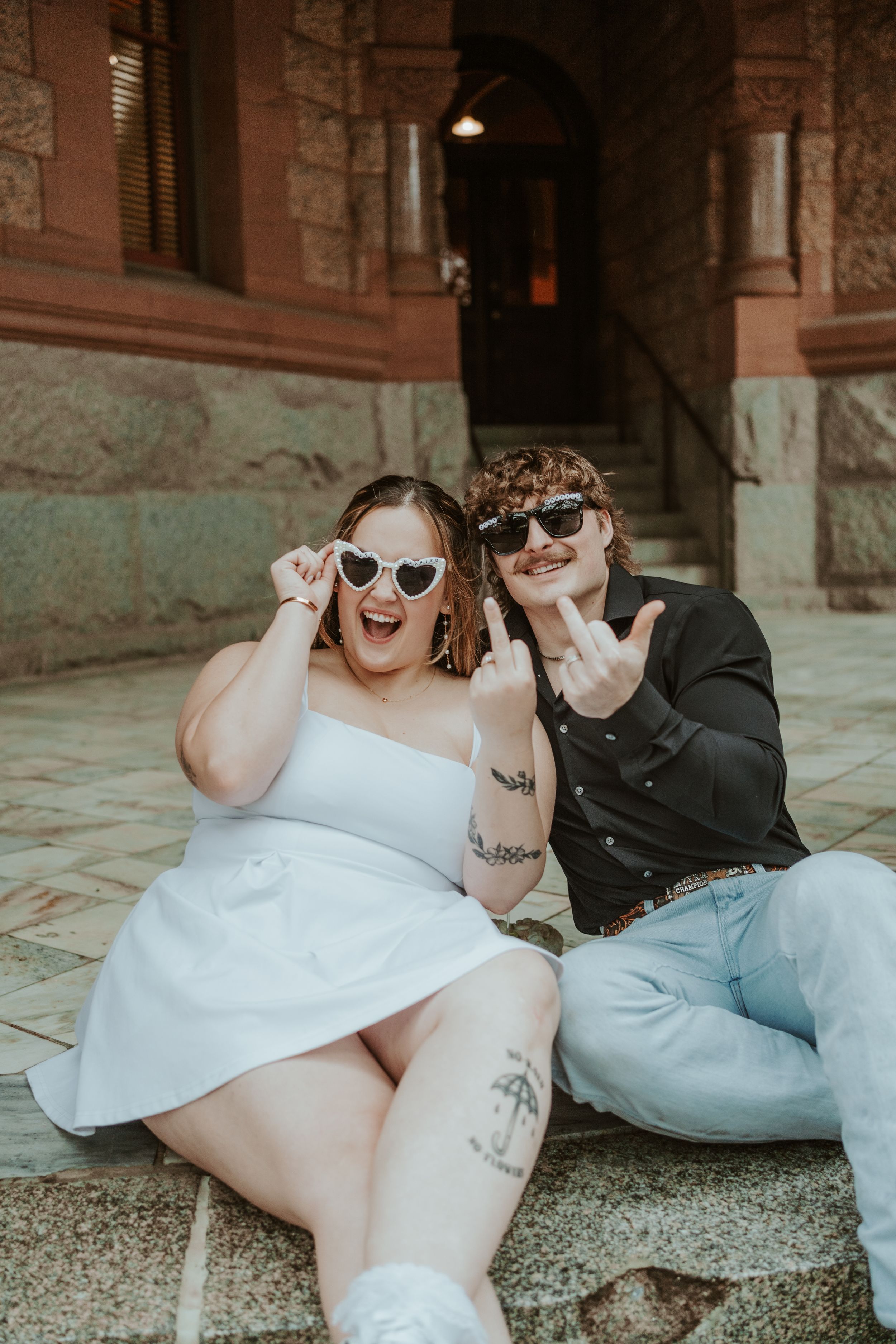 Two people lounging on stone steps wearing sunglasses in casual attire.