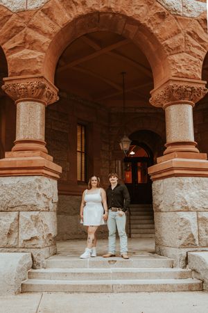 Couple sitting on stone steps of historic building with arched columns.