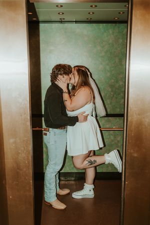 A couple sharing a tender kiss in an elevator with a mint green wall background.