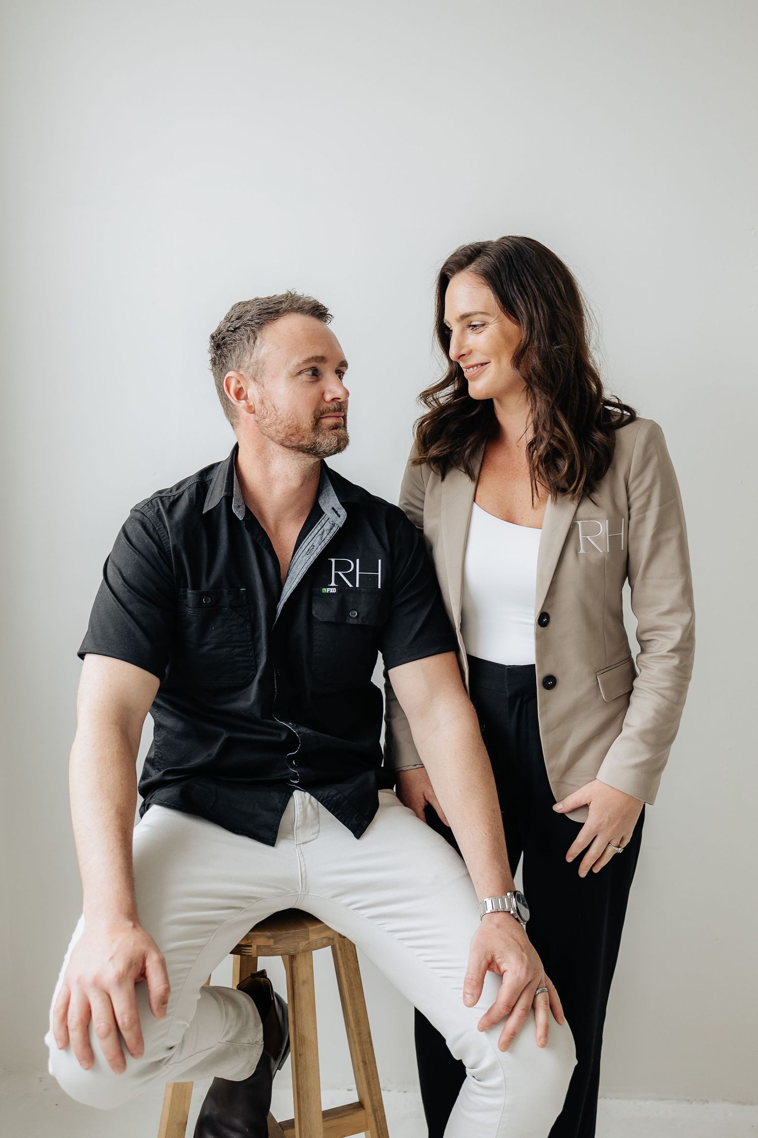 Two professionals collaborating while seated on wooden stools against white backdrop.