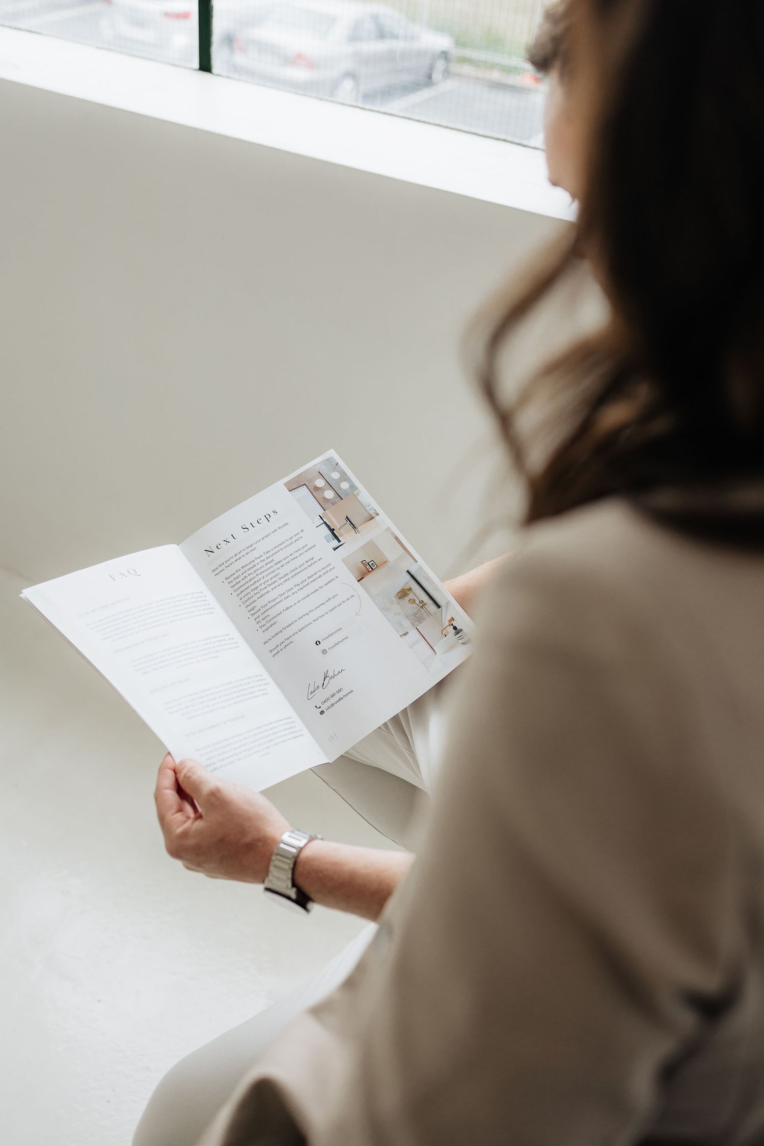 Person in beige blazer reviews printed business documents in modern office setting.