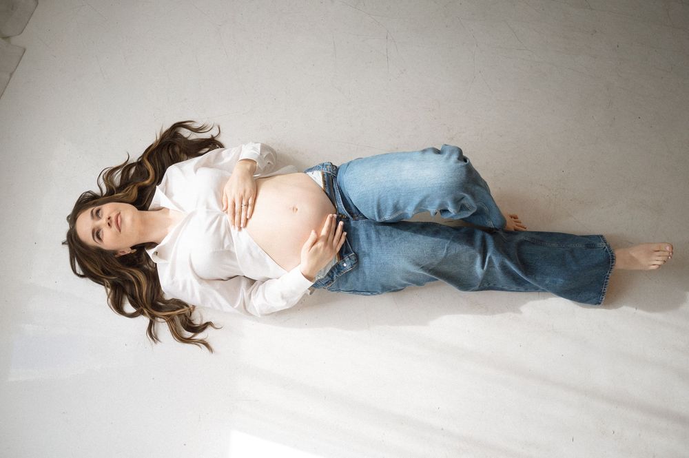 Person in white shirt and jeans lying on floor in artistic poses against light gray background.