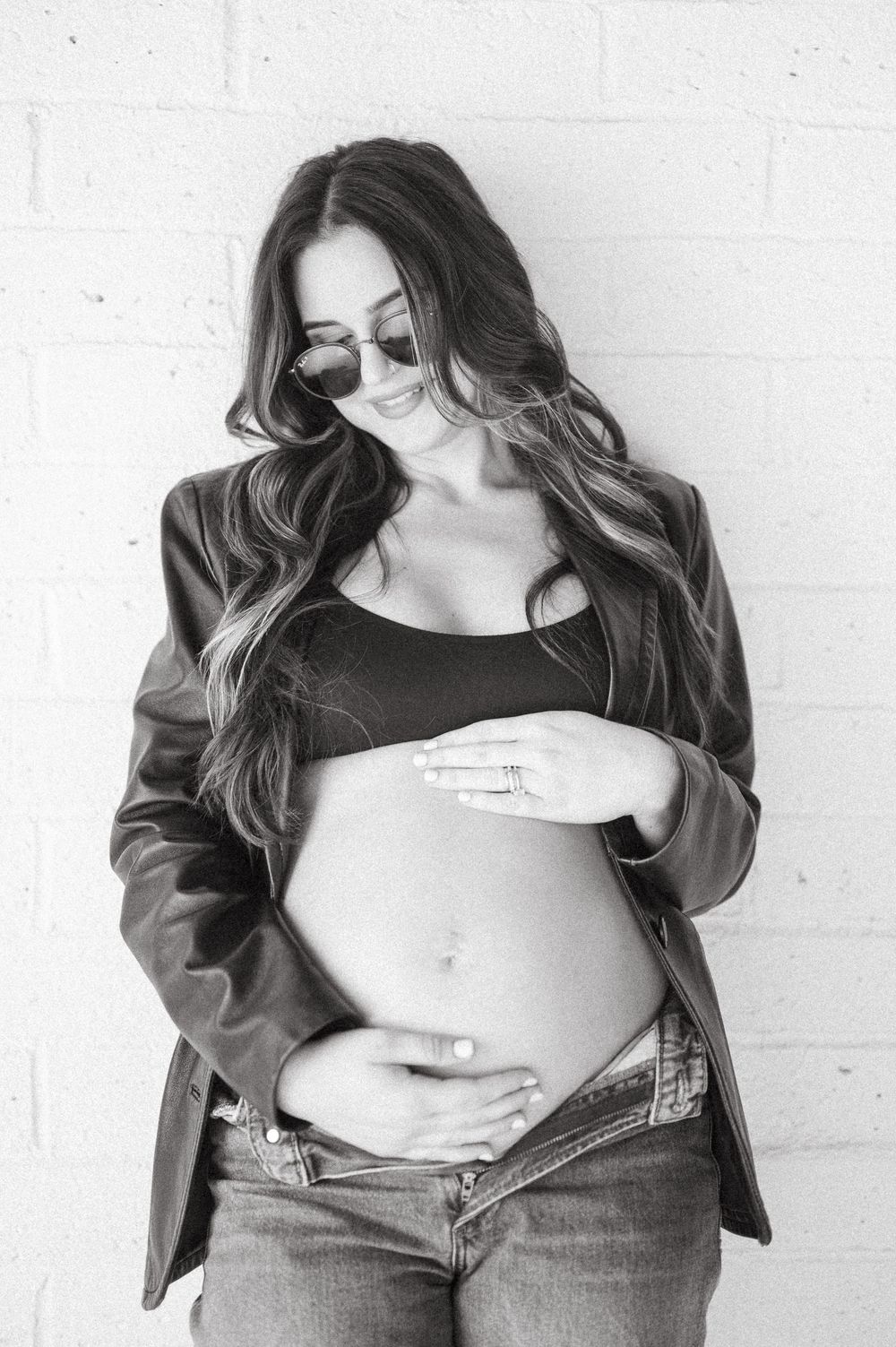 A series of black and white maternity photos showing a pregnant belly against a white brick wall background.