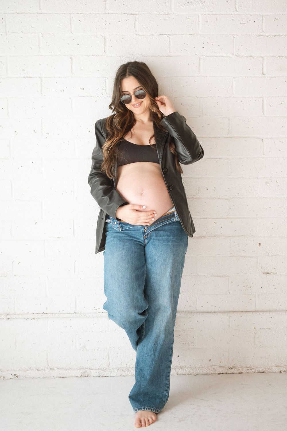 Maternity photo sequence showing pregnant woman in denim and black jacket against white brick wall.