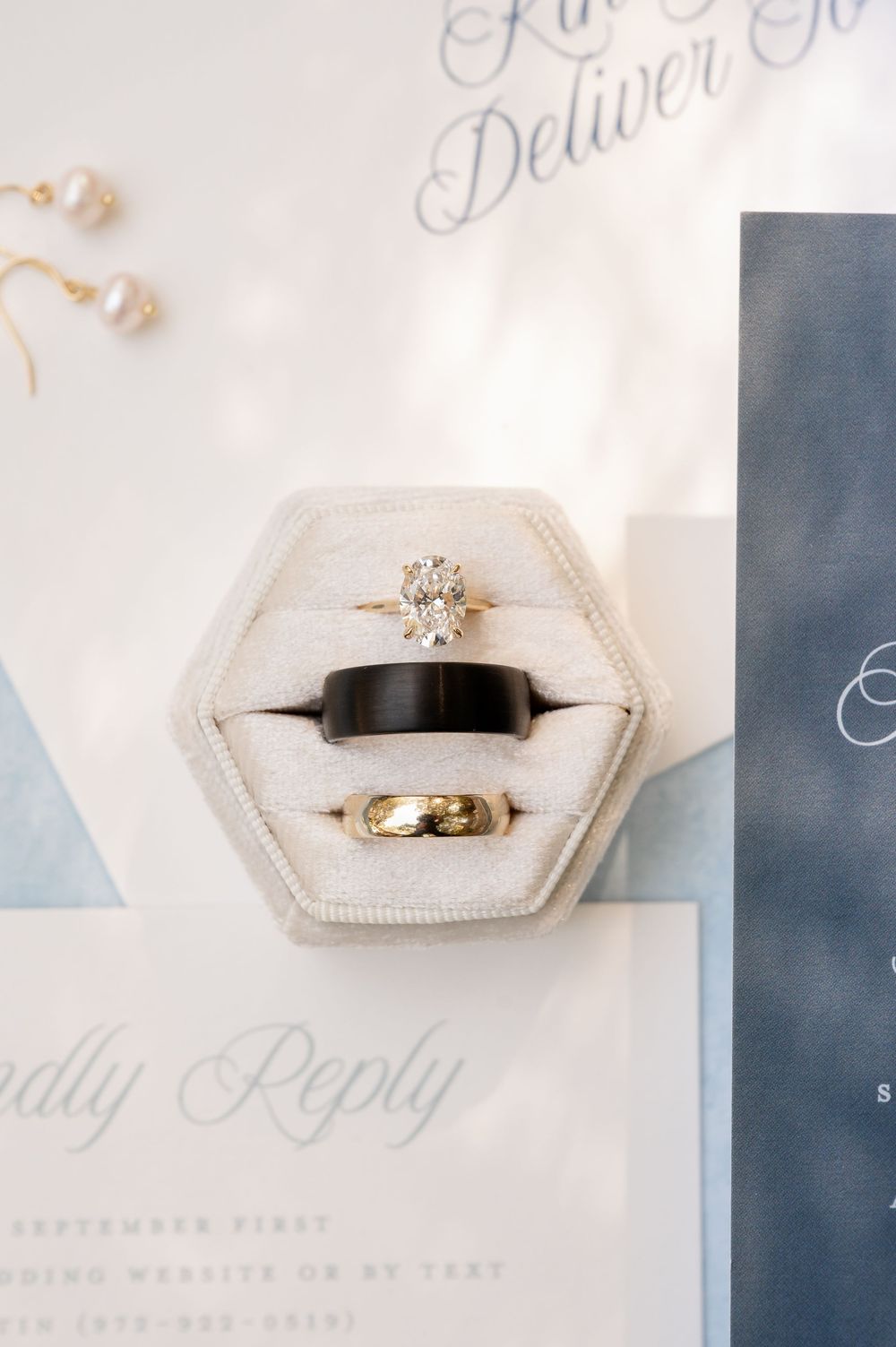 Wedding rings displayed in elegant hexagonal ring boxes against a light blue and white invitation suite.