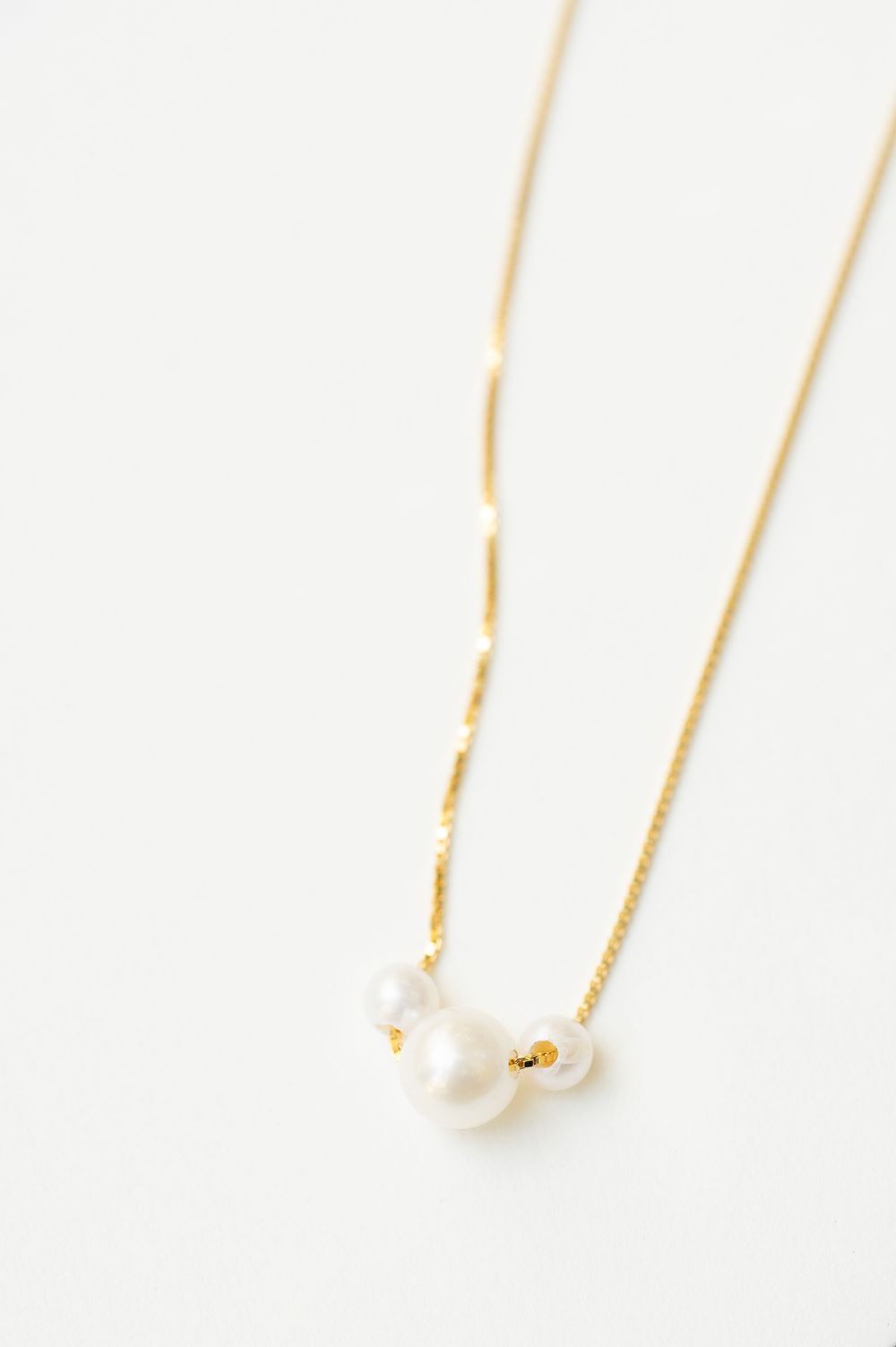 Delicate gold chain necklace with pearl details on white background.
