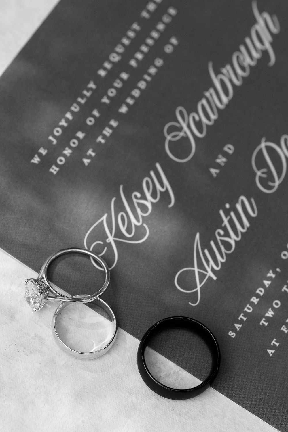 Wedding rings photographed on dark invitation with elegant calligraphy.