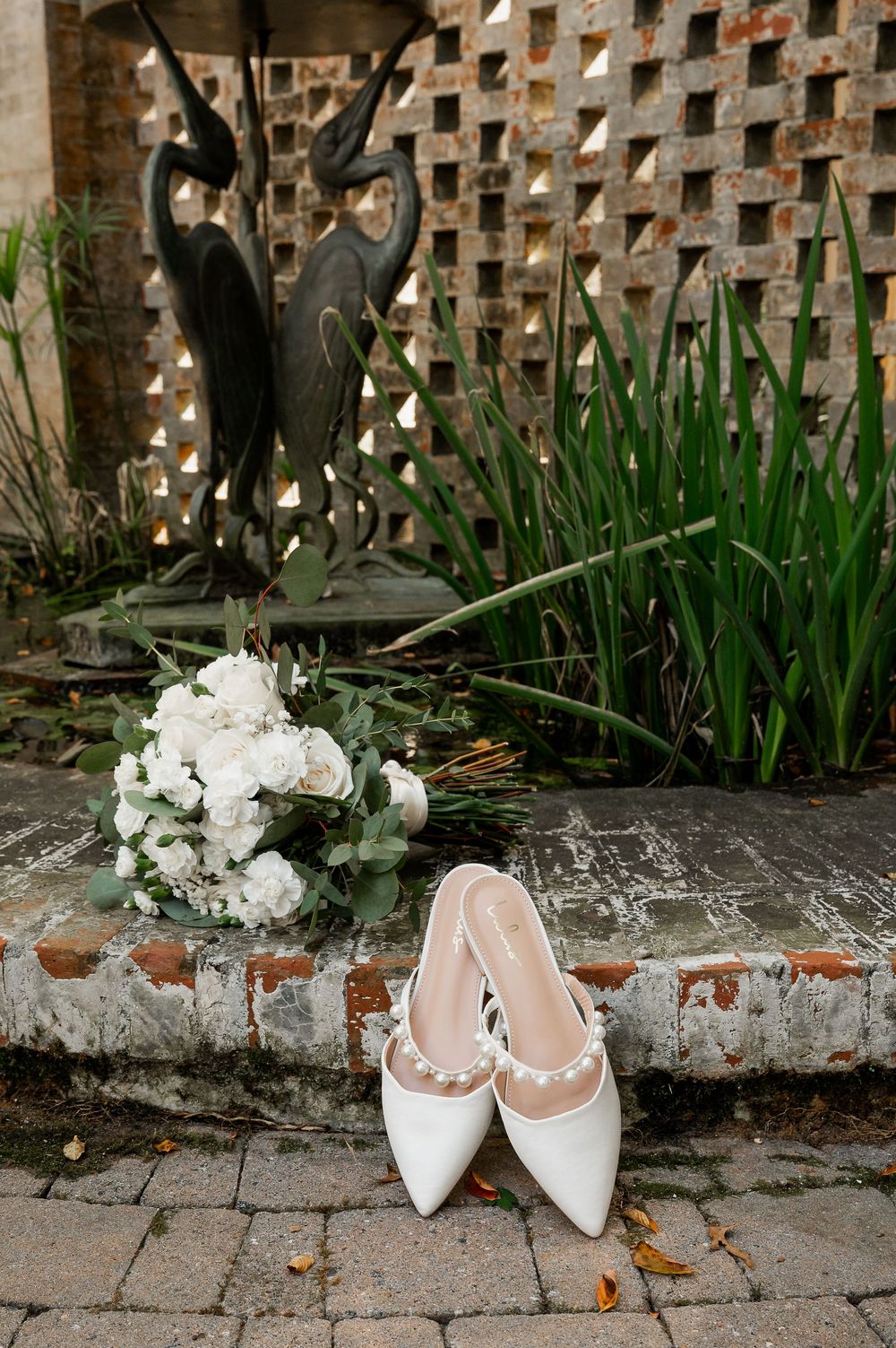 White bridal shoes arranged with floral details against a rustic brick wall.
