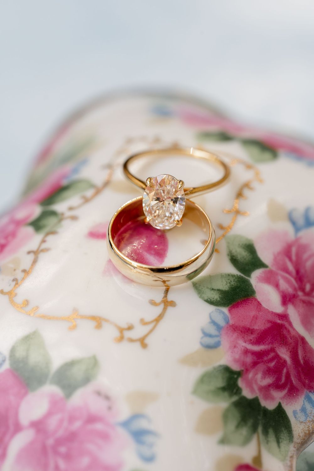 Gold engagement ring with diamond solitaire displayed on vintage floral china.