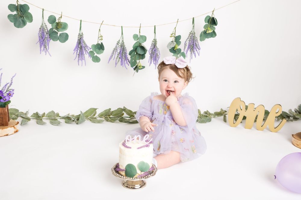 A delicate floral arrangement with eucalyptus leaves and purple flowers creates an ethereal composition against a white backdrop.