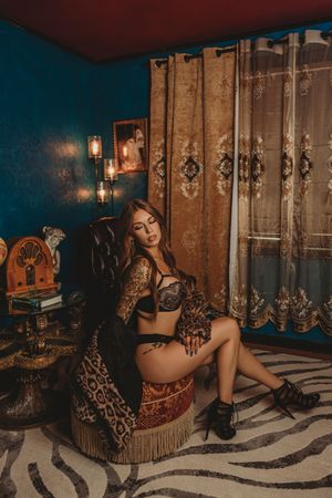 Moody boudoir scene with vintage decor featuring ornate curtains, zebra rug and antique furniture in dim lighting.