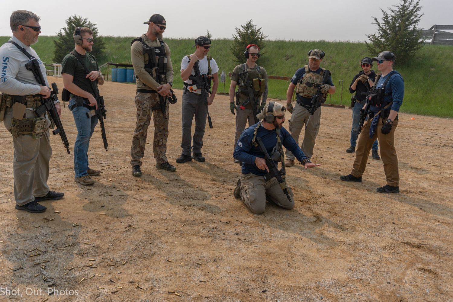 Group of armed individuals in tactical gear participating in outdoor firearms training on a dirt range.