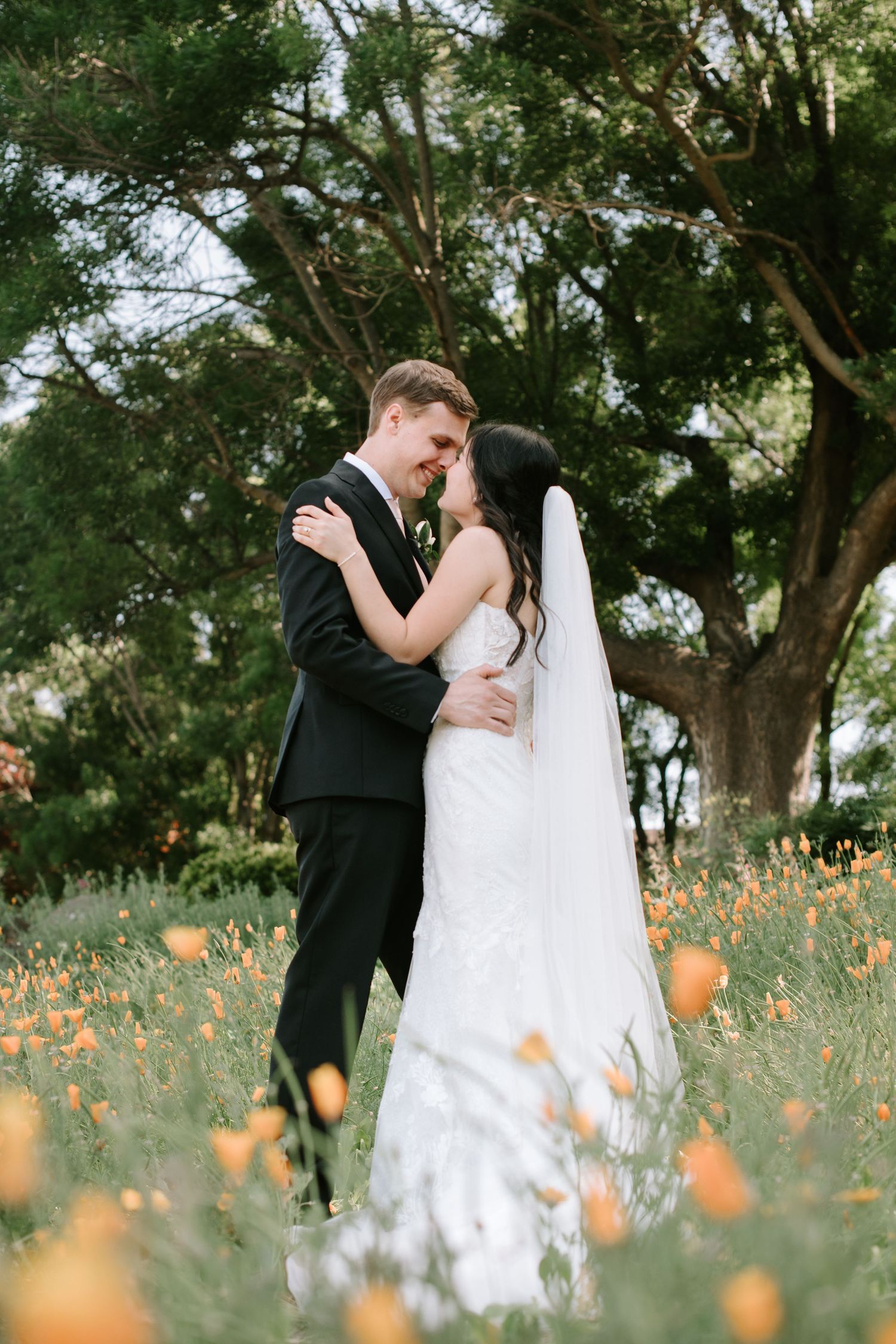 Newlywed couple shares romantic moments in a meadow filled with delicate orange wildflowers on their wedding day.