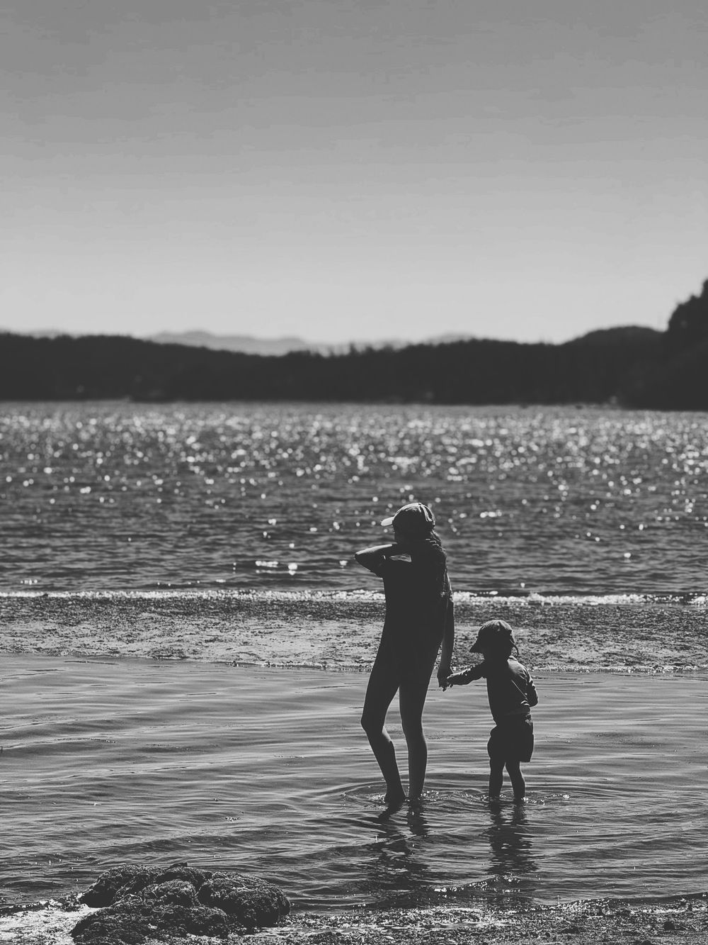 Silhouettes of two people standing in shallow water at sunset with sparkling reflections on the lake surface.