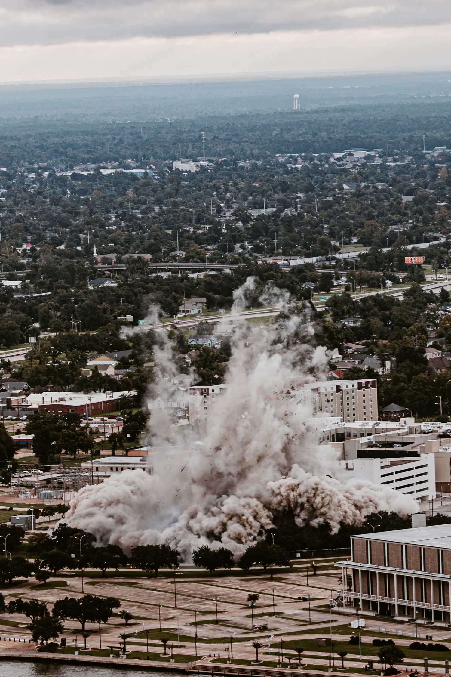 Aerial view of building demolition with large dust cloud spreading across urban landscape.