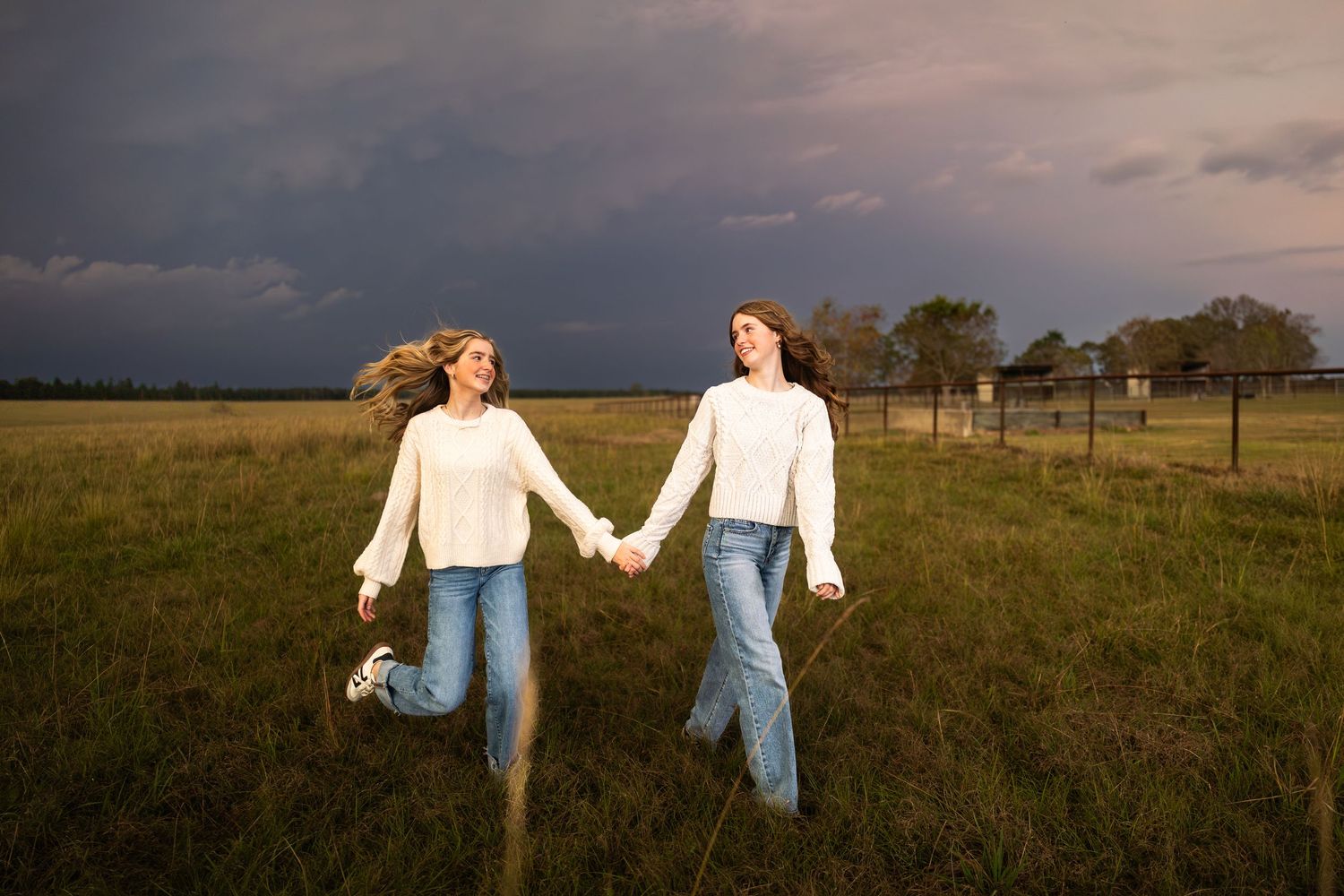 People walking through a grassy field at sunset holding hands in casual outfits.