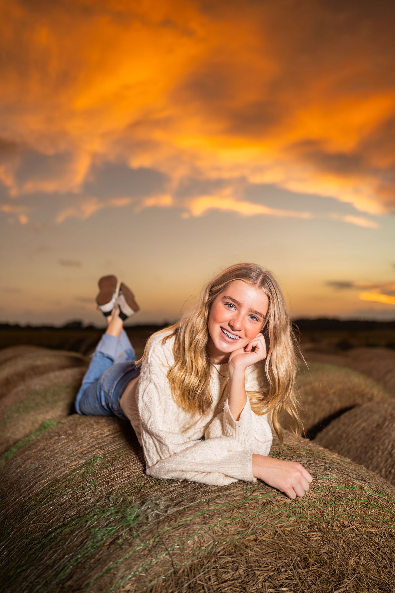 Portrait session on hay bales during golden hour sunset in countryside setting.