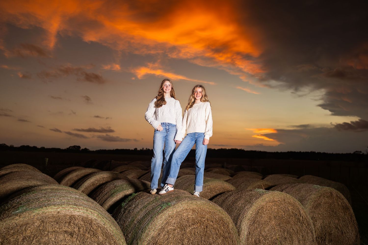 Silhouettes standing on hay bales at sunset in rural farm field.