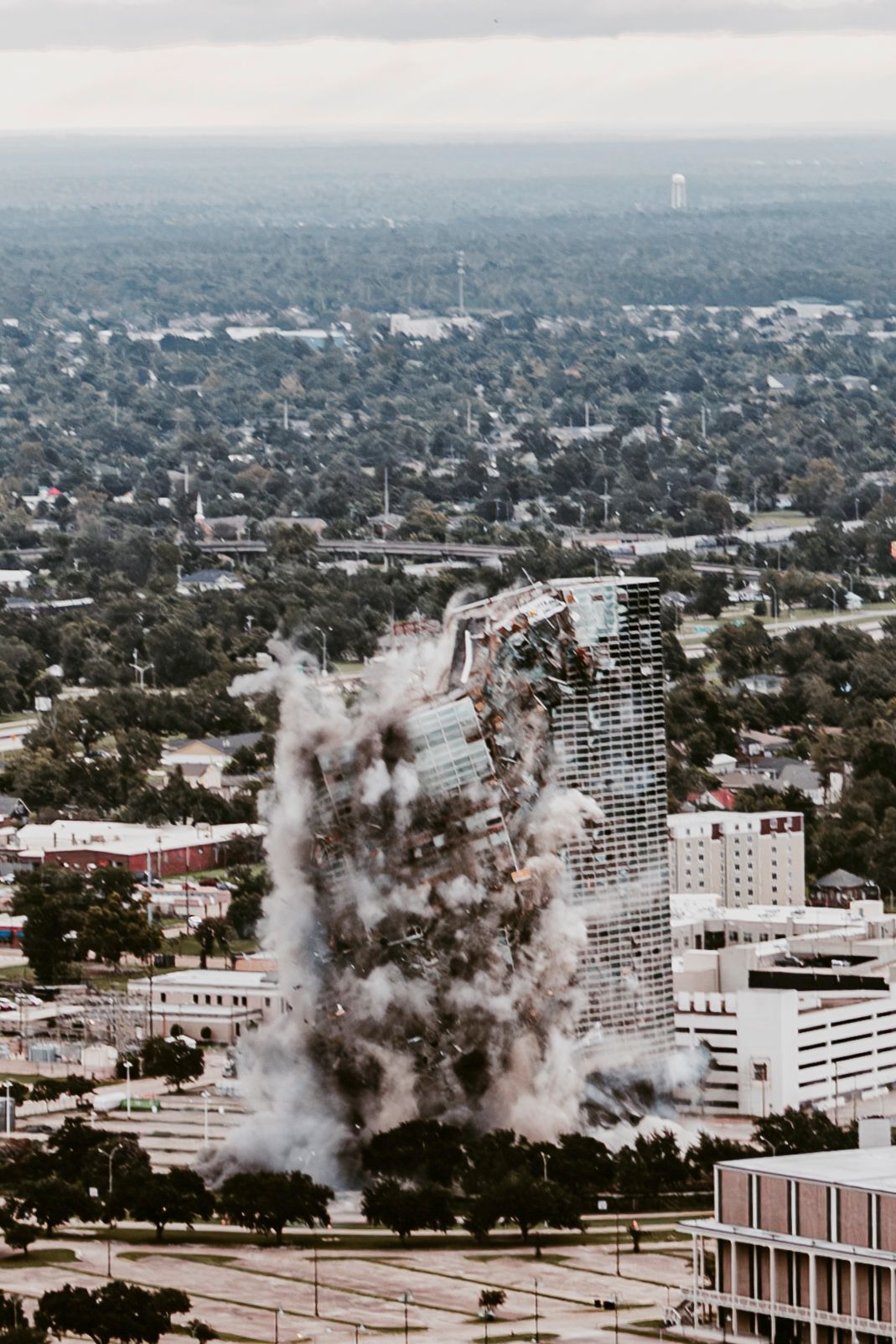 Sequence showing the controlled demolition of a large urban building with rising dust clouds.