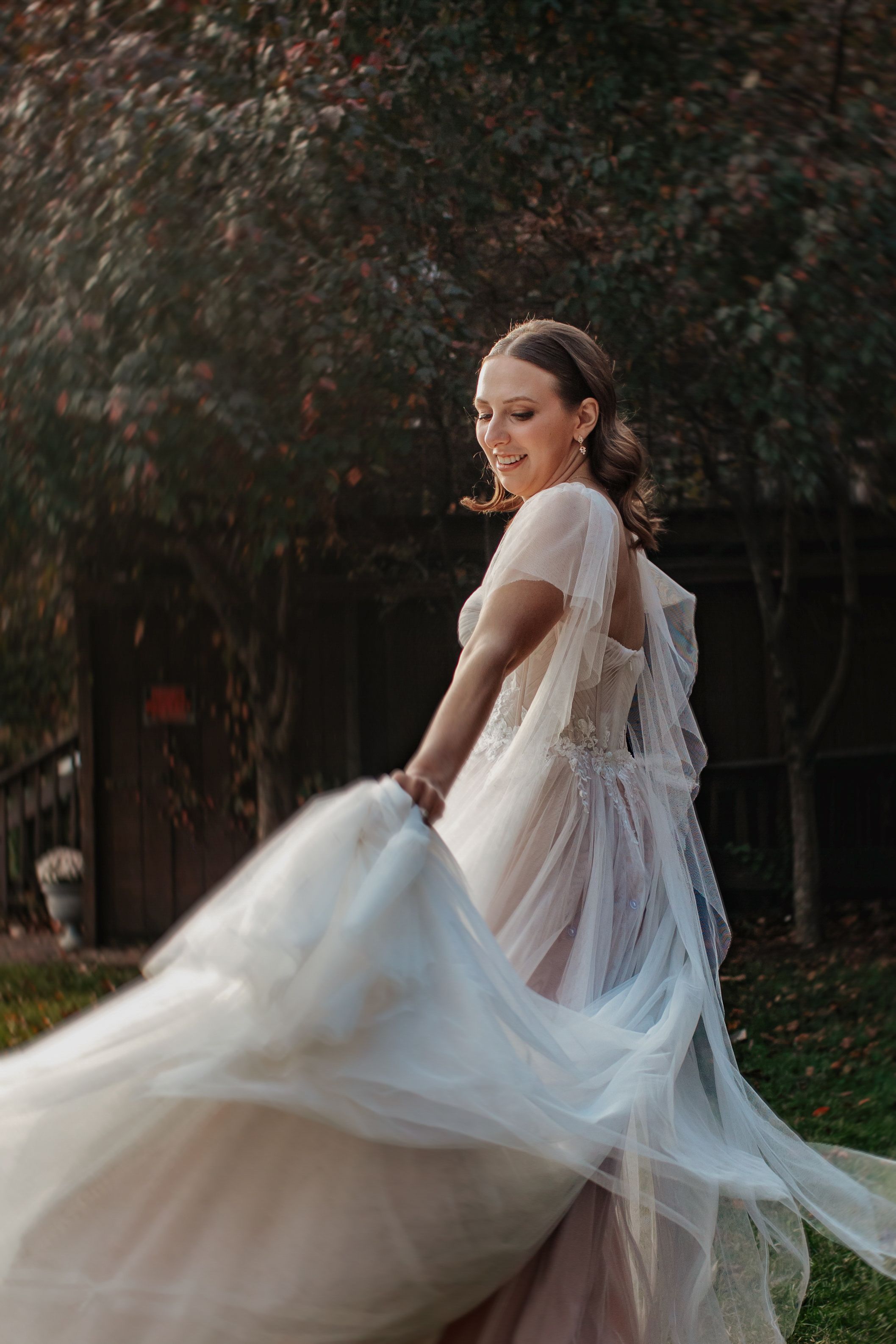 A bride in a flowing white gown twirls gracefully in a garden setting, creating ethereal movement with her dress.