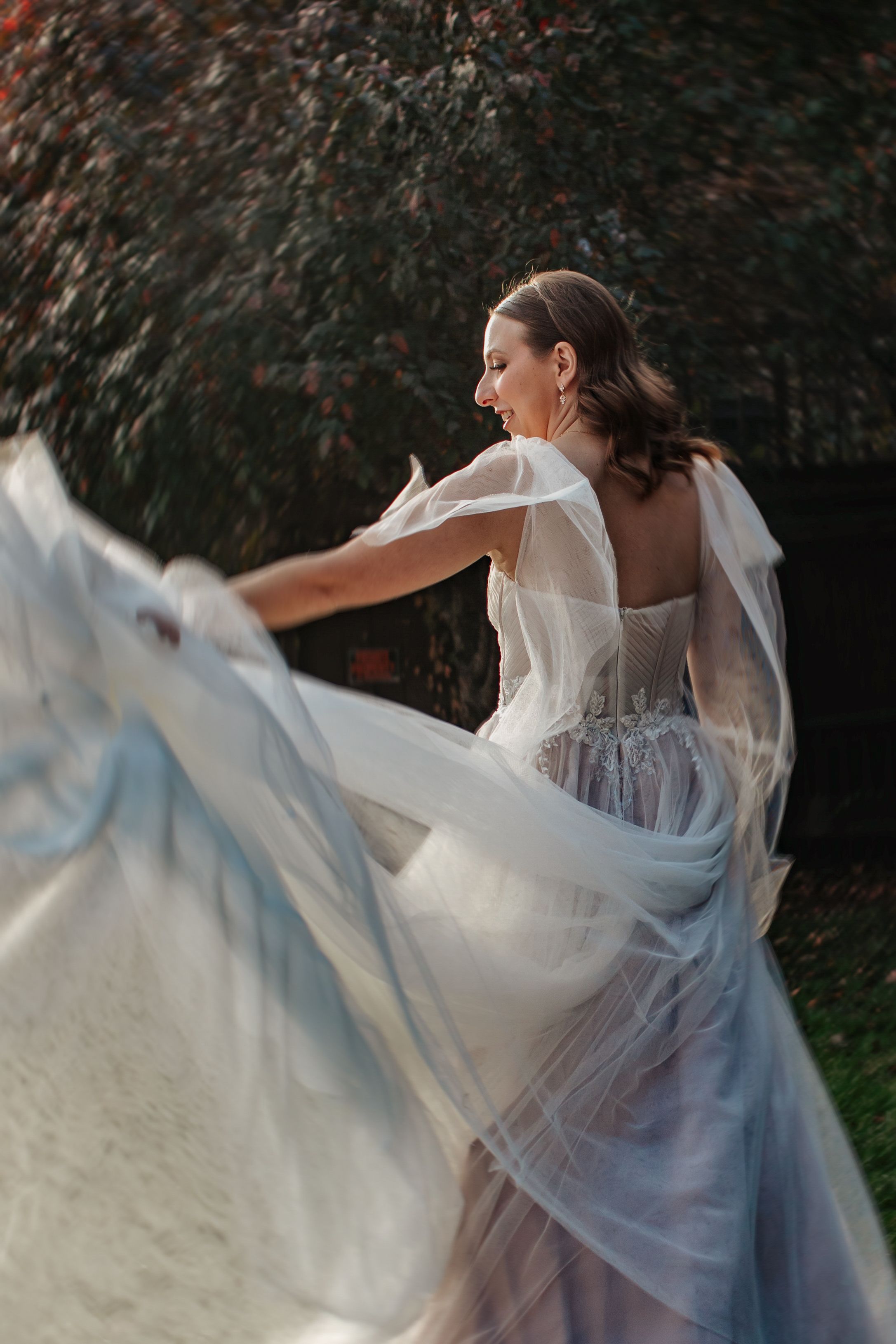 A flowing white dress billows gracefully in the wind as a figure twirls in an outdoor garden setting.
