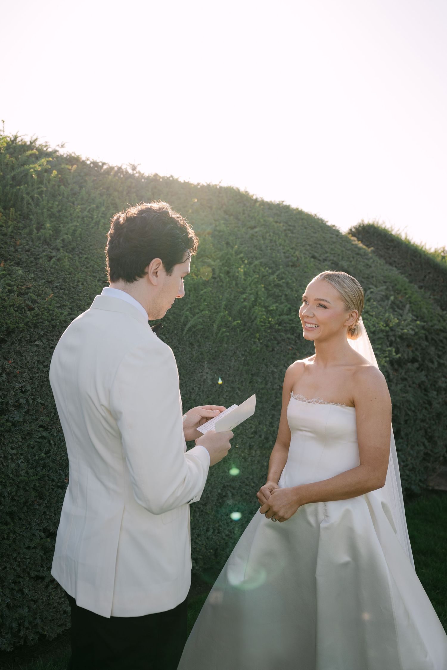 Couple poses elegantly in formal attire near glass pyramid architecture in romantic wedding photoshoot.