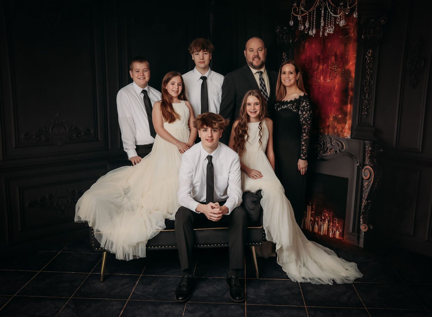 Wedding group sits together on vintage furniture in dramatic dark room with red accent lighting.