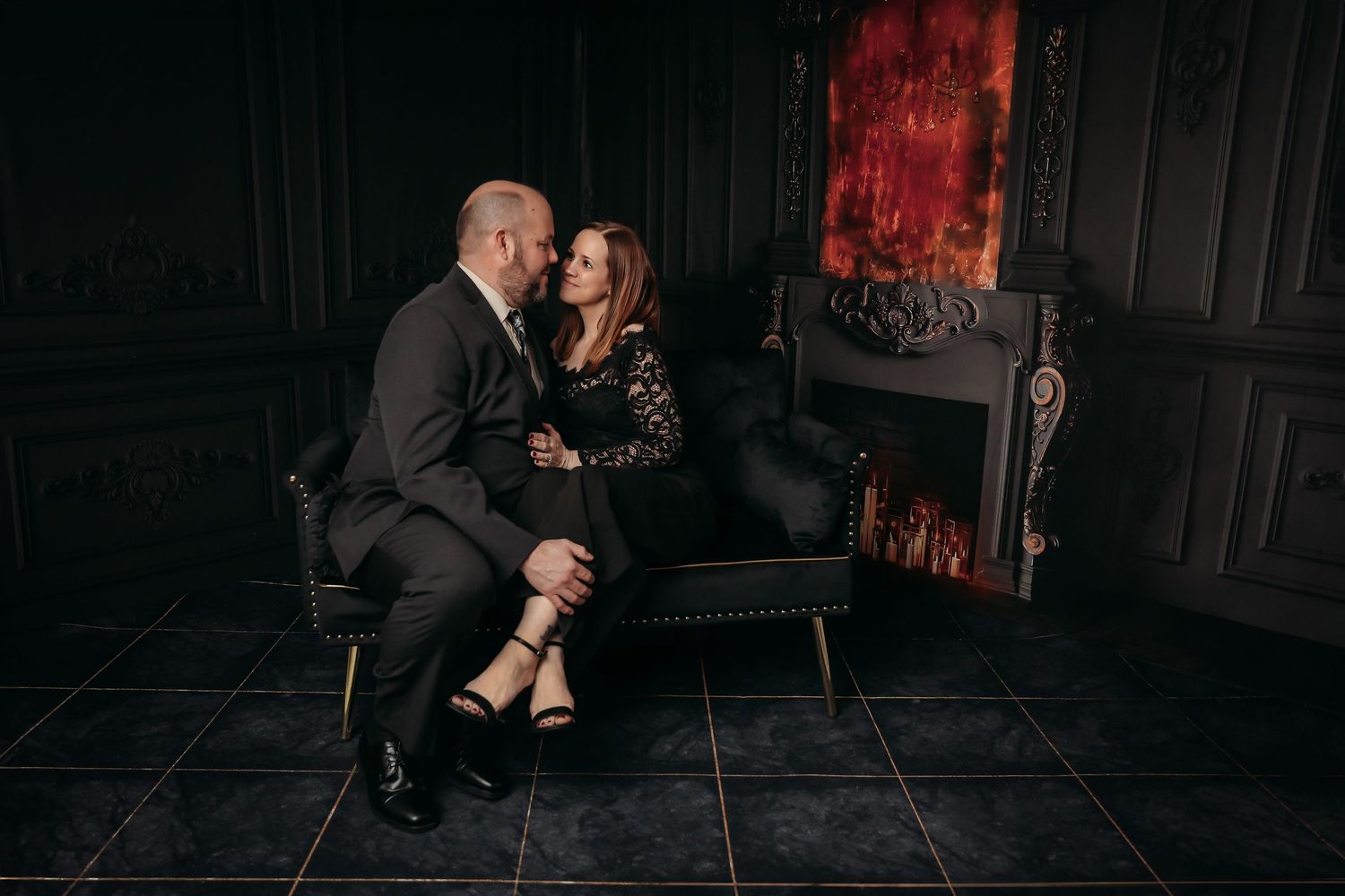 A couple in formal attire dances together in a dimly lit room with dramatic red lighting and dark shadows.