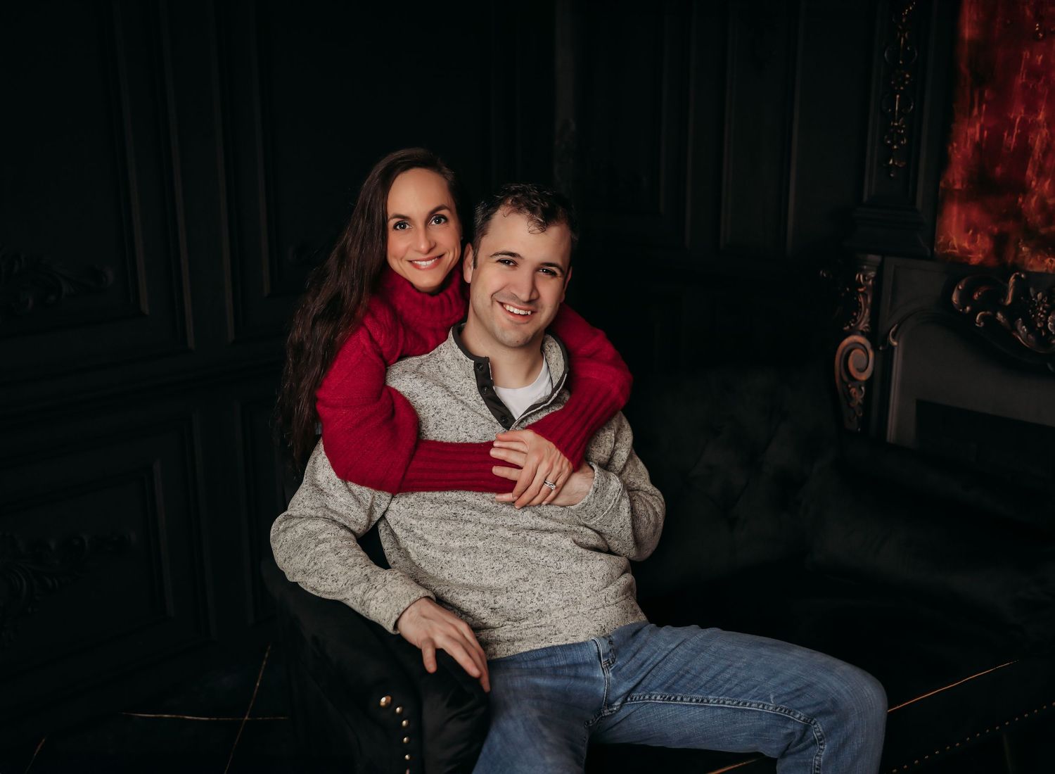A couple sits together on a couch in a dimly lit room sharing an intimate moment.