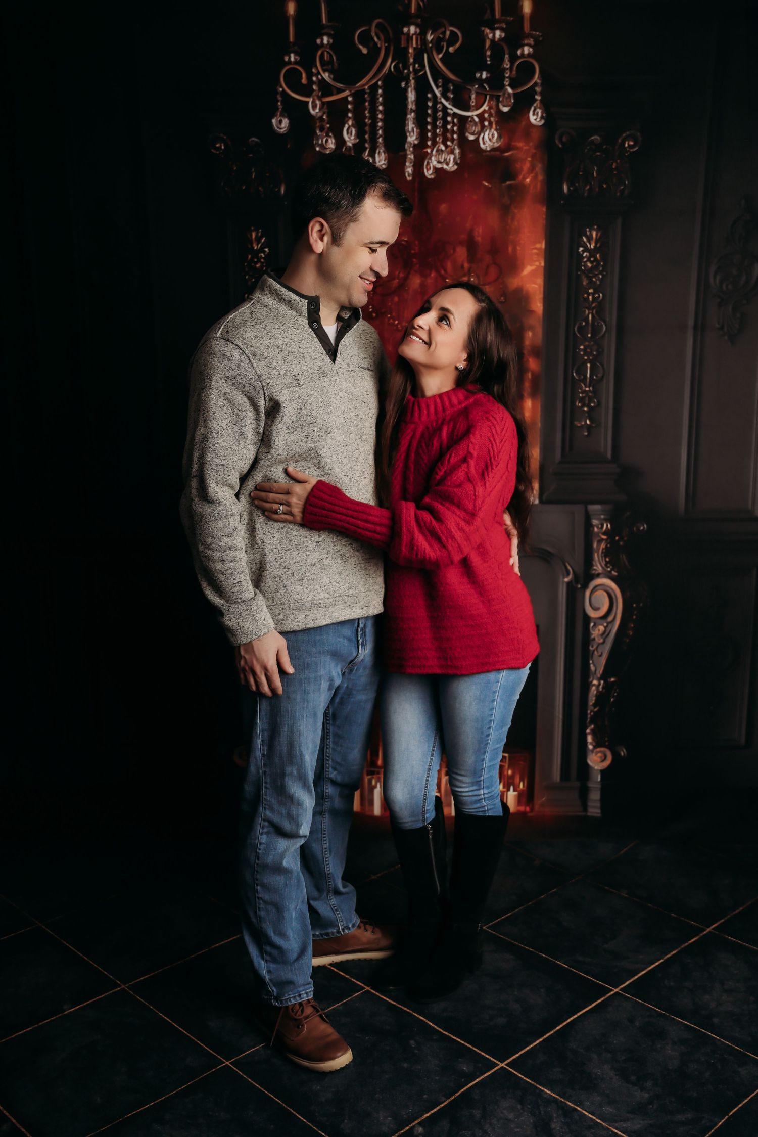 A couple in jeans and sweaters share an intimate moment in a dark, moody setting with ornate decor.