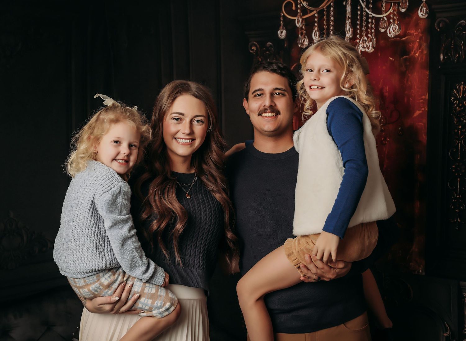 A family poses together in a series of five dark moody portraits with warm lighting and black backgrounds.