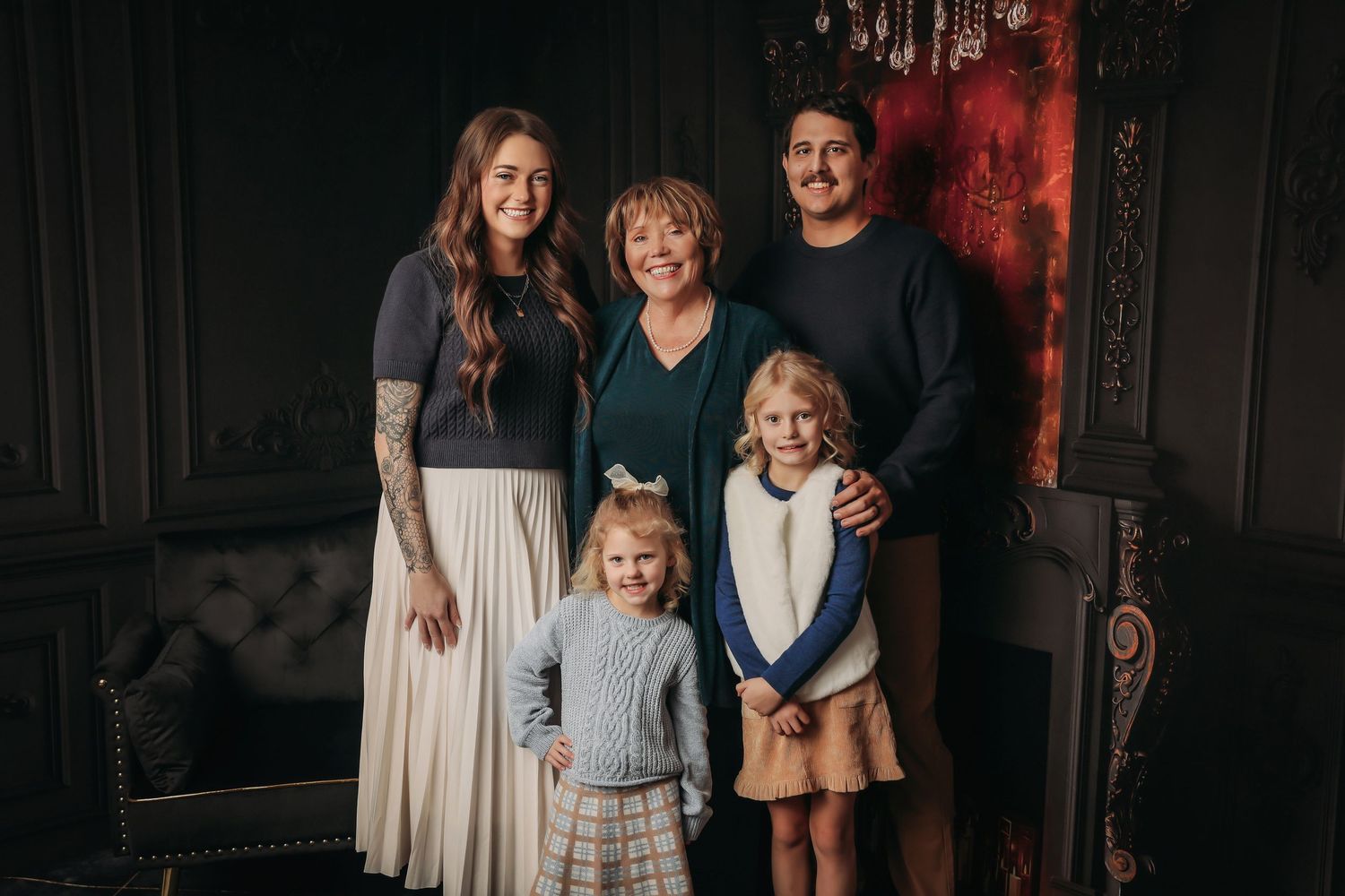 A family poses together in a dark studio with dramatic red lighting against a black background.