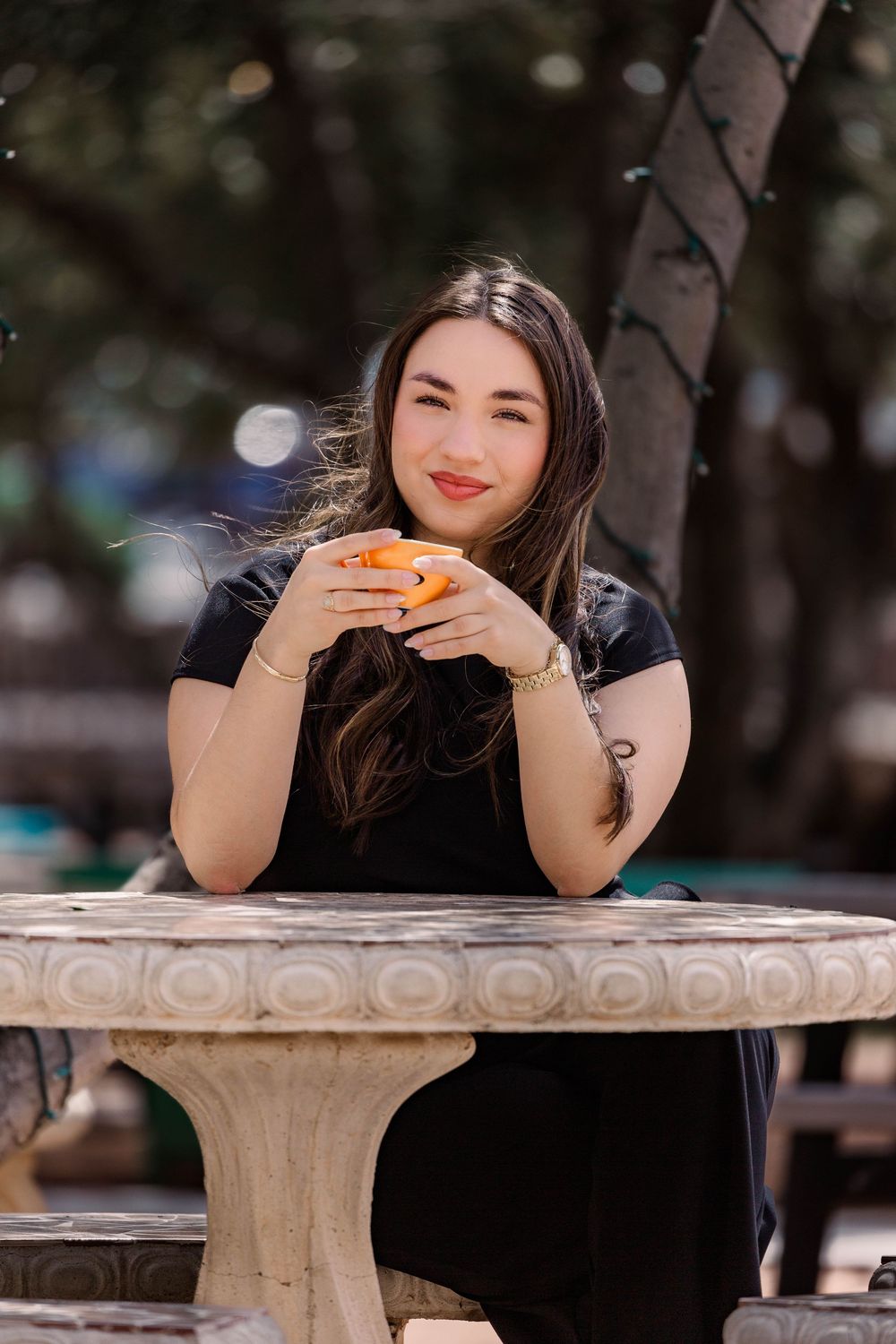 A candid outdoor photo of someone in black enjoying food at a decorative stone table.