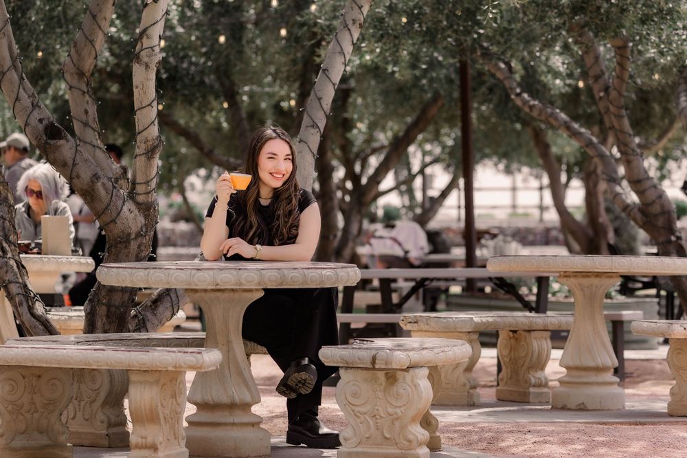 Students study and socialize at outdoor tables on a college campus surrounded by trees.