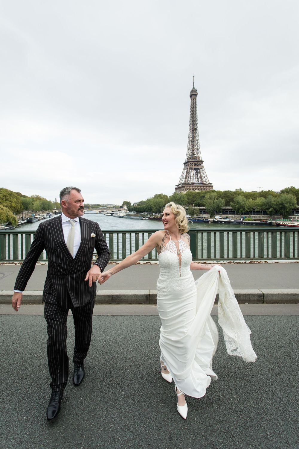 A couple dances playfully on a bridge with the iconic Eiffel Tower visible in the background in Paris.