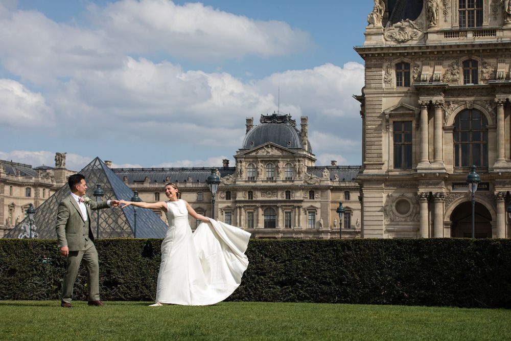 A wedding couple poses for romantic photos in front of the historic Louvre Museum in Paris. They are dancing celabrating their Elopement