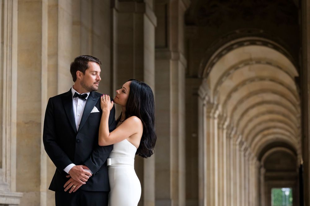 Elegant wedding couple shares romantic moments in front of ornate stone archways and columns at the Louvre
