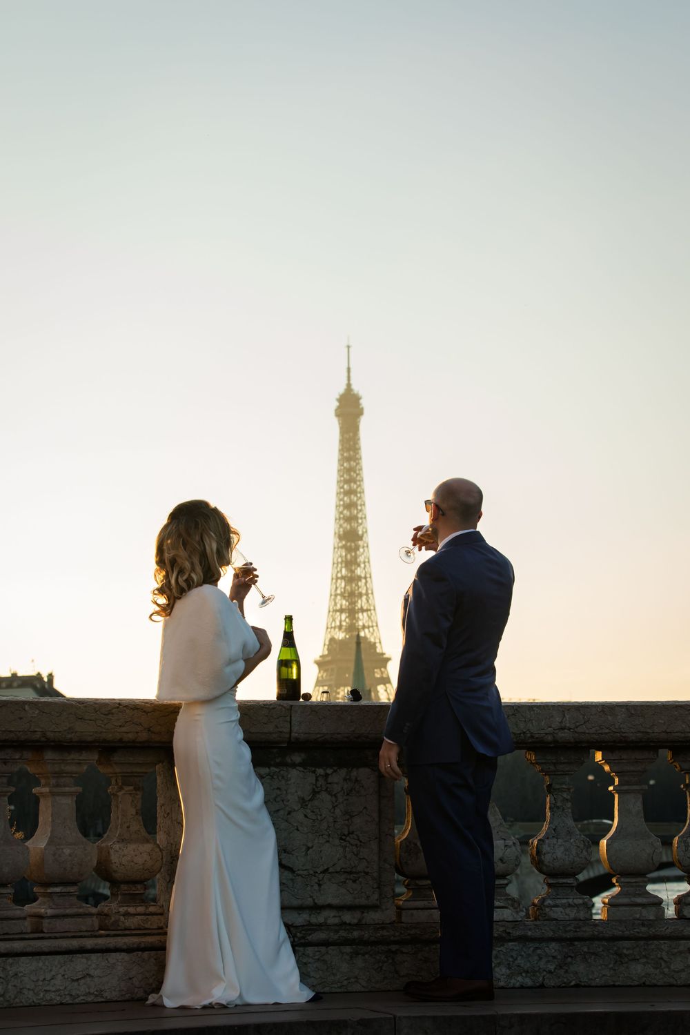 A couple shares champagne on a balcony overlooking the Eiffel Tower at sunset in Paris, captured by Julien LB Photography Paris