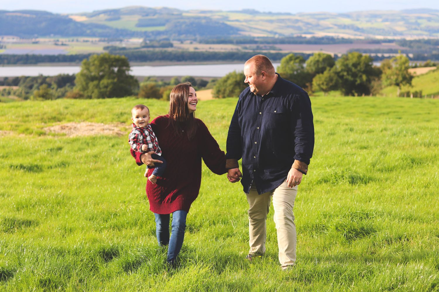 Family walking together through a lush green hillside meadow on a sunny afternoon.