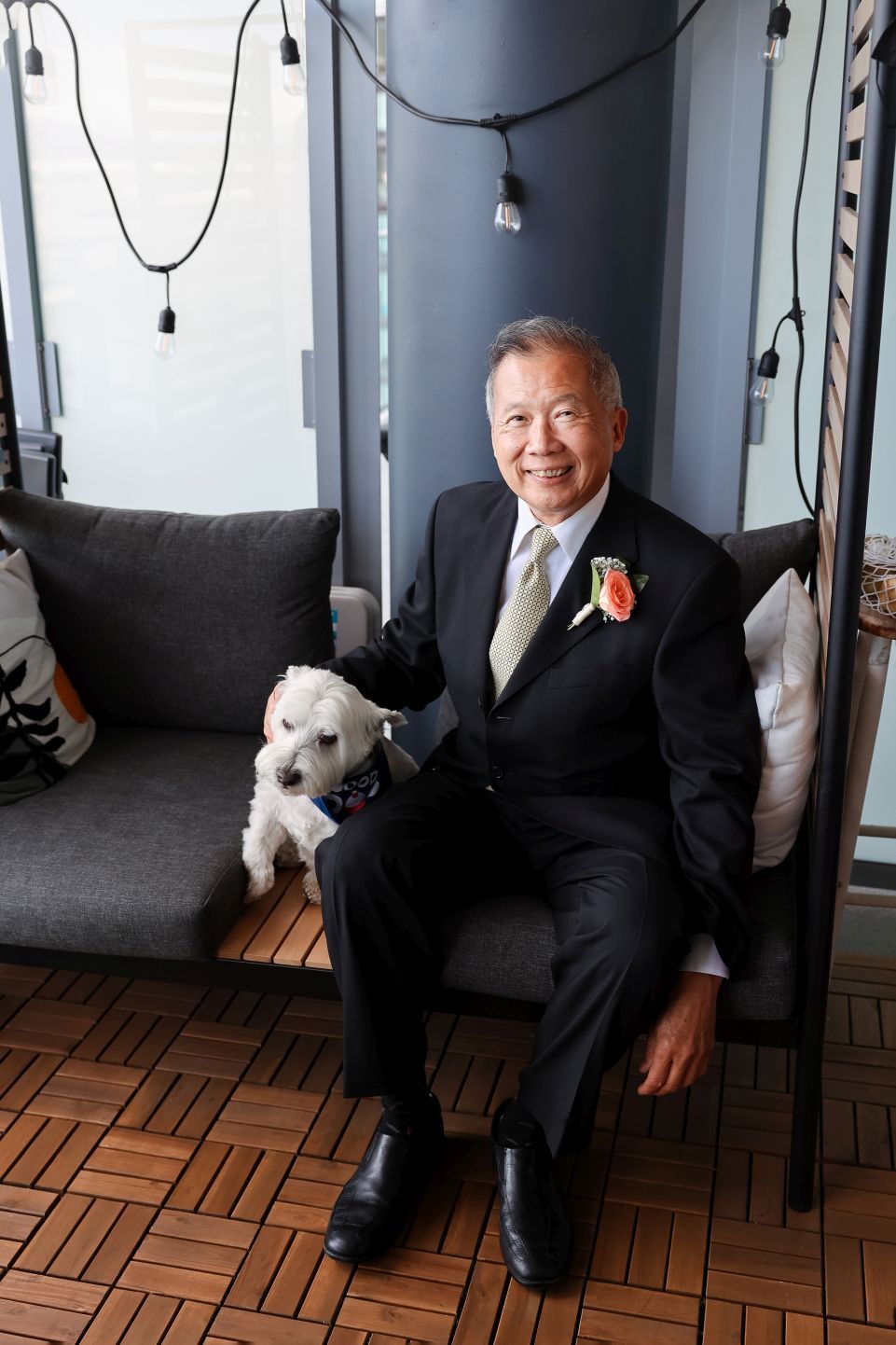 A smartly dressed couple poses on a couch with a small white dog during a special occasion.