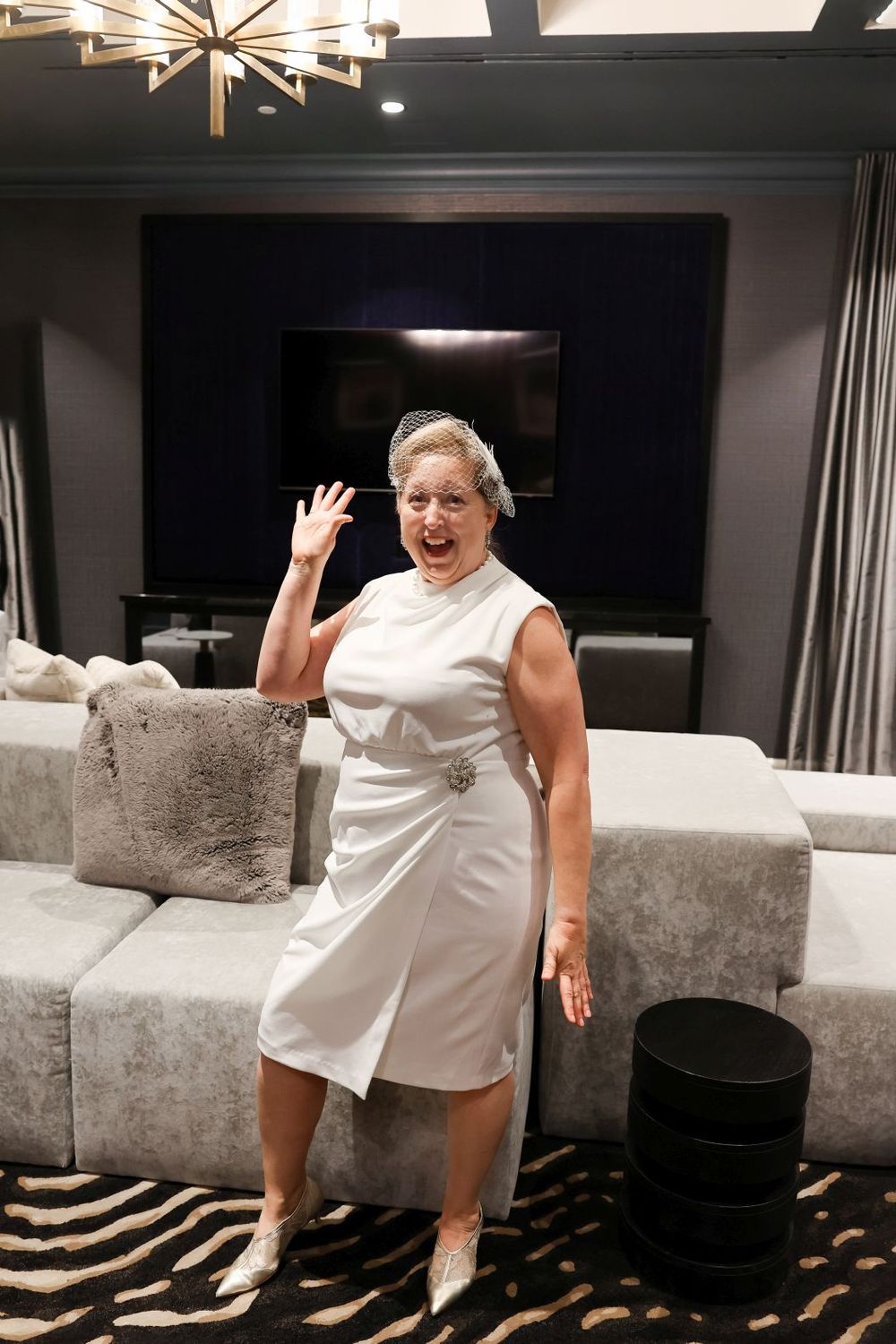 Someone in a white dress poses enthusiastically in an elegantly decorated room with modern furniture.