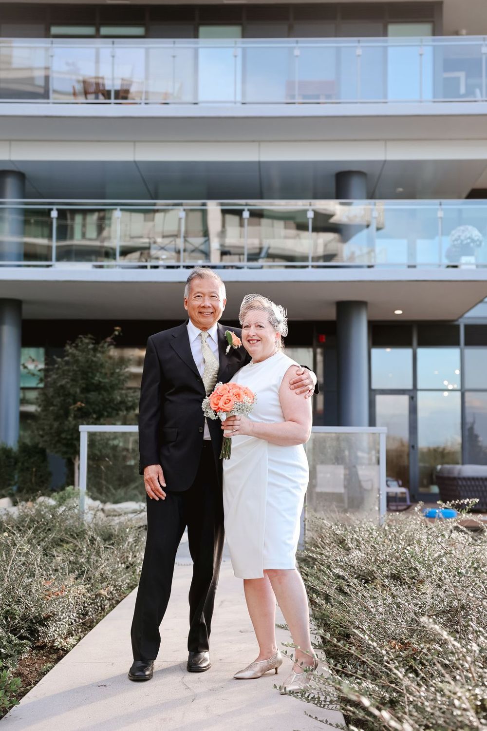 A couple stands together on a pathway outside a modern building during a celebration.