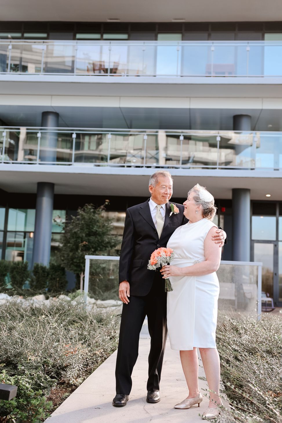 A happy couple shares a joyful moment outside a modern glass building.