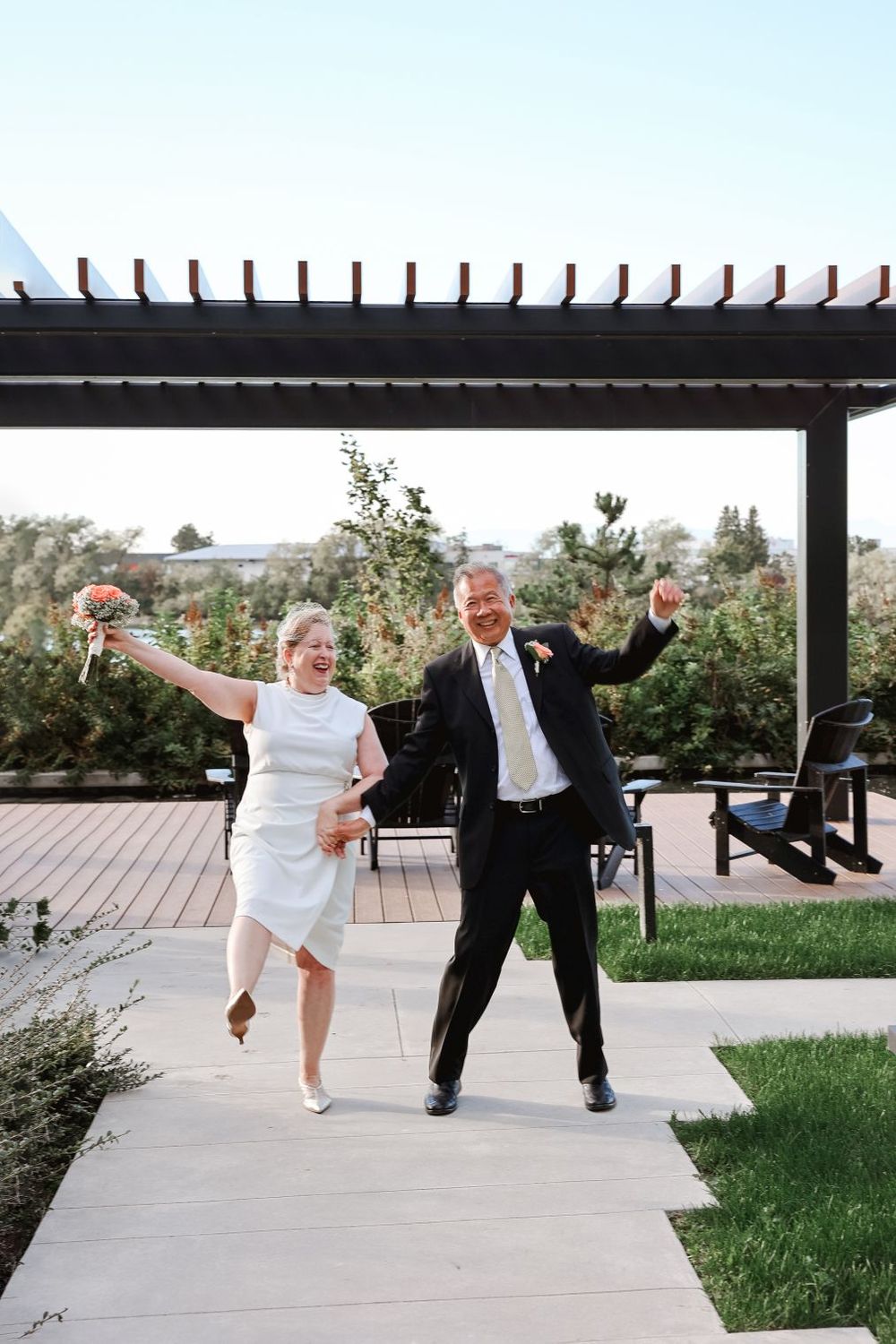 A couple dances joyfully on an outdoor patio under a pergola.