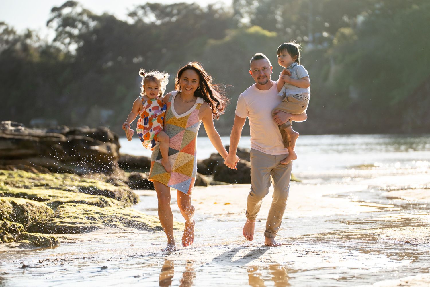 Family of four running towards the camera on a beach at golden hour, capturing joyful moments during a family photoshoot