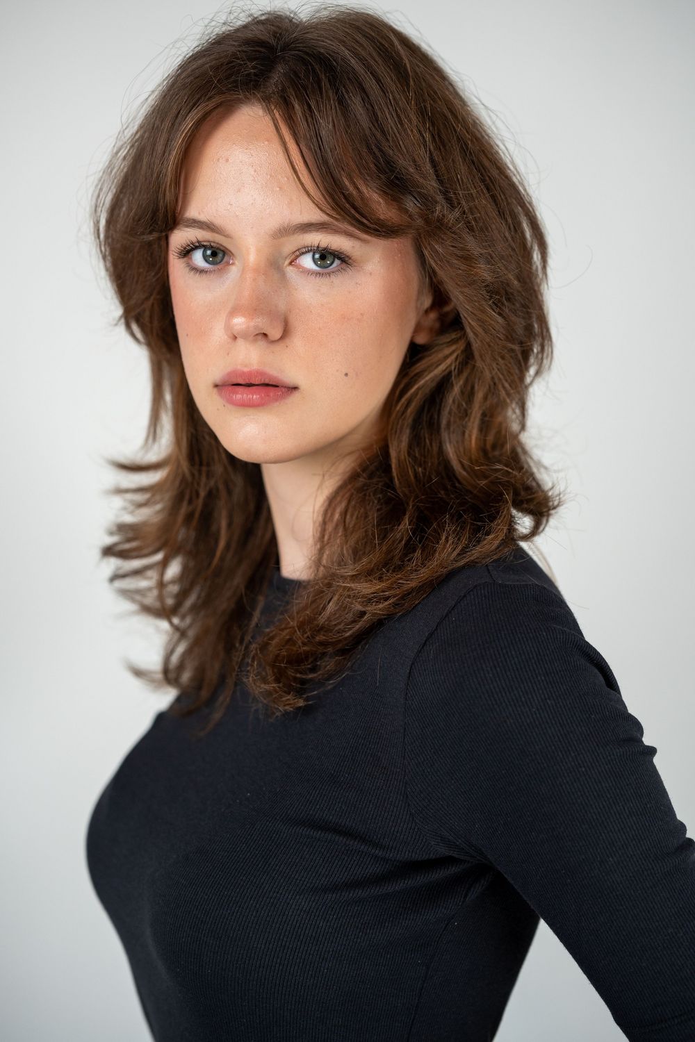 Portrait series of person with layered brown hair wearing a black top against white background.