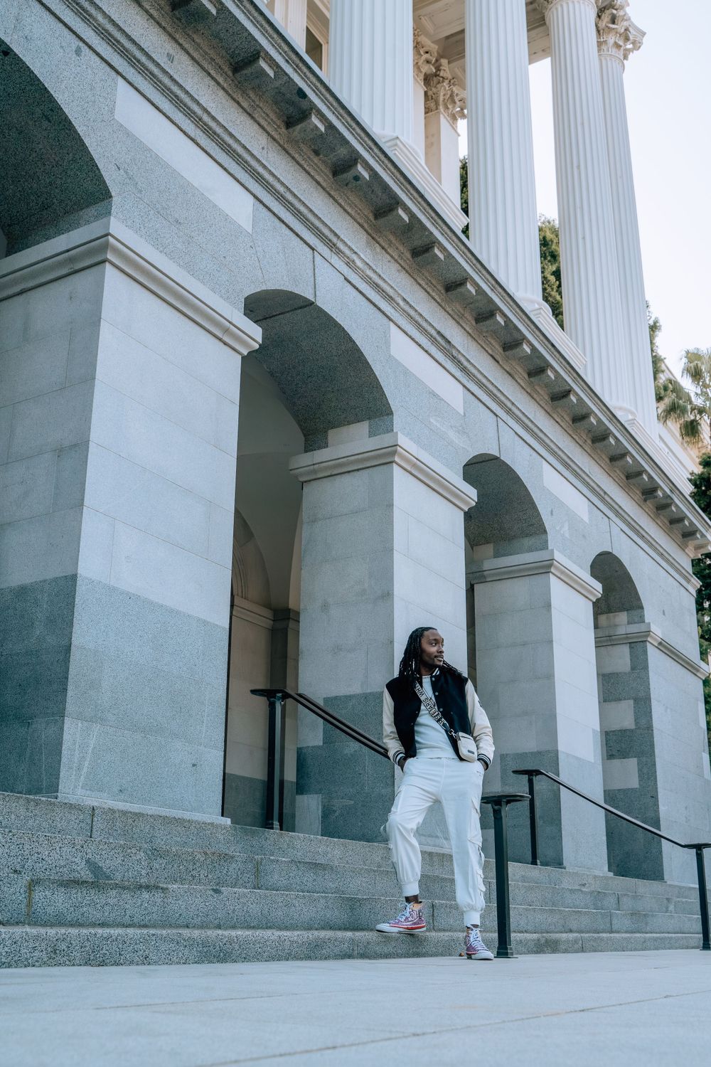 Figure in black and white outfit posing artistically against classical architecture with columns.