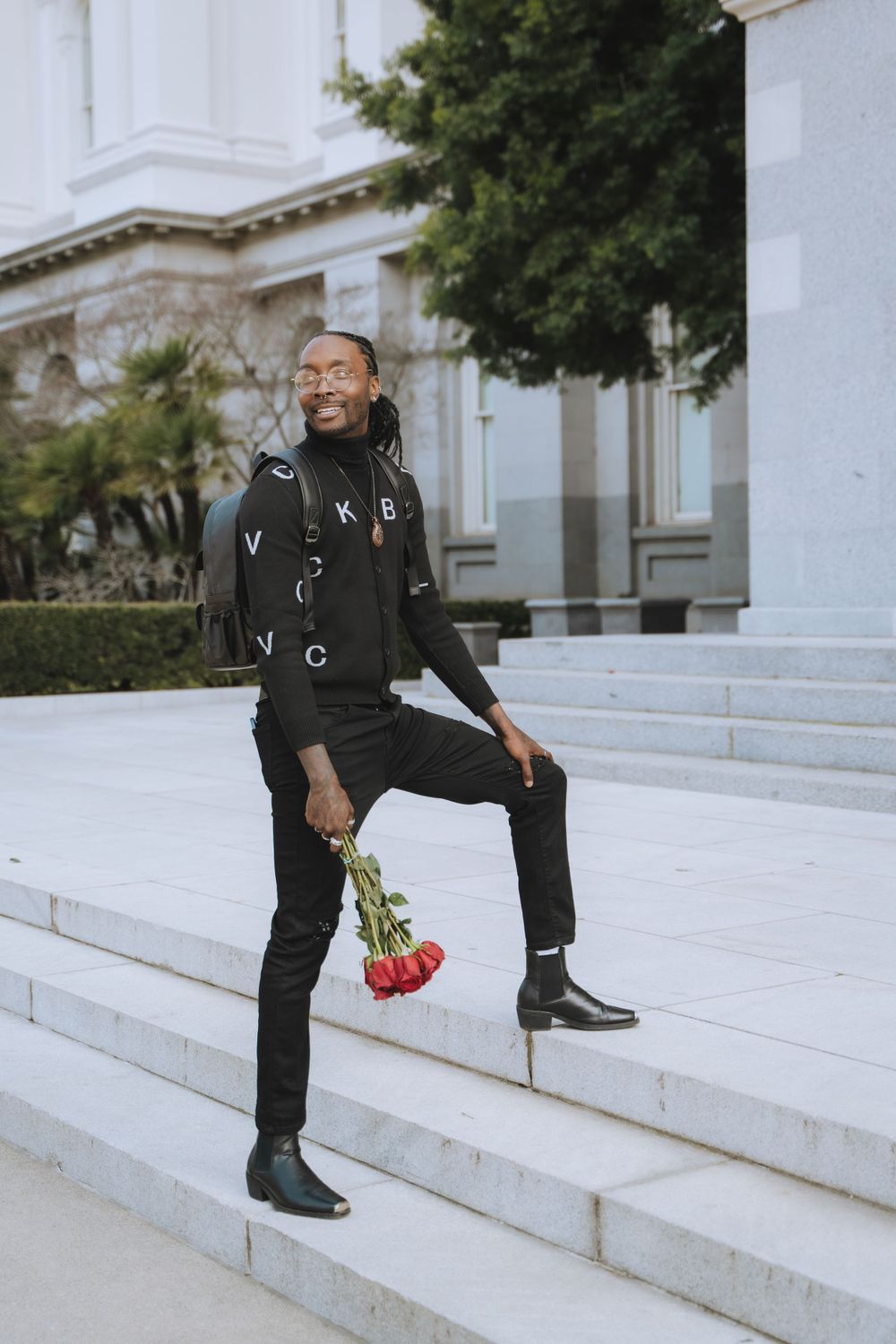 Person in black attire posing with flowers on white marble steps outdoors.