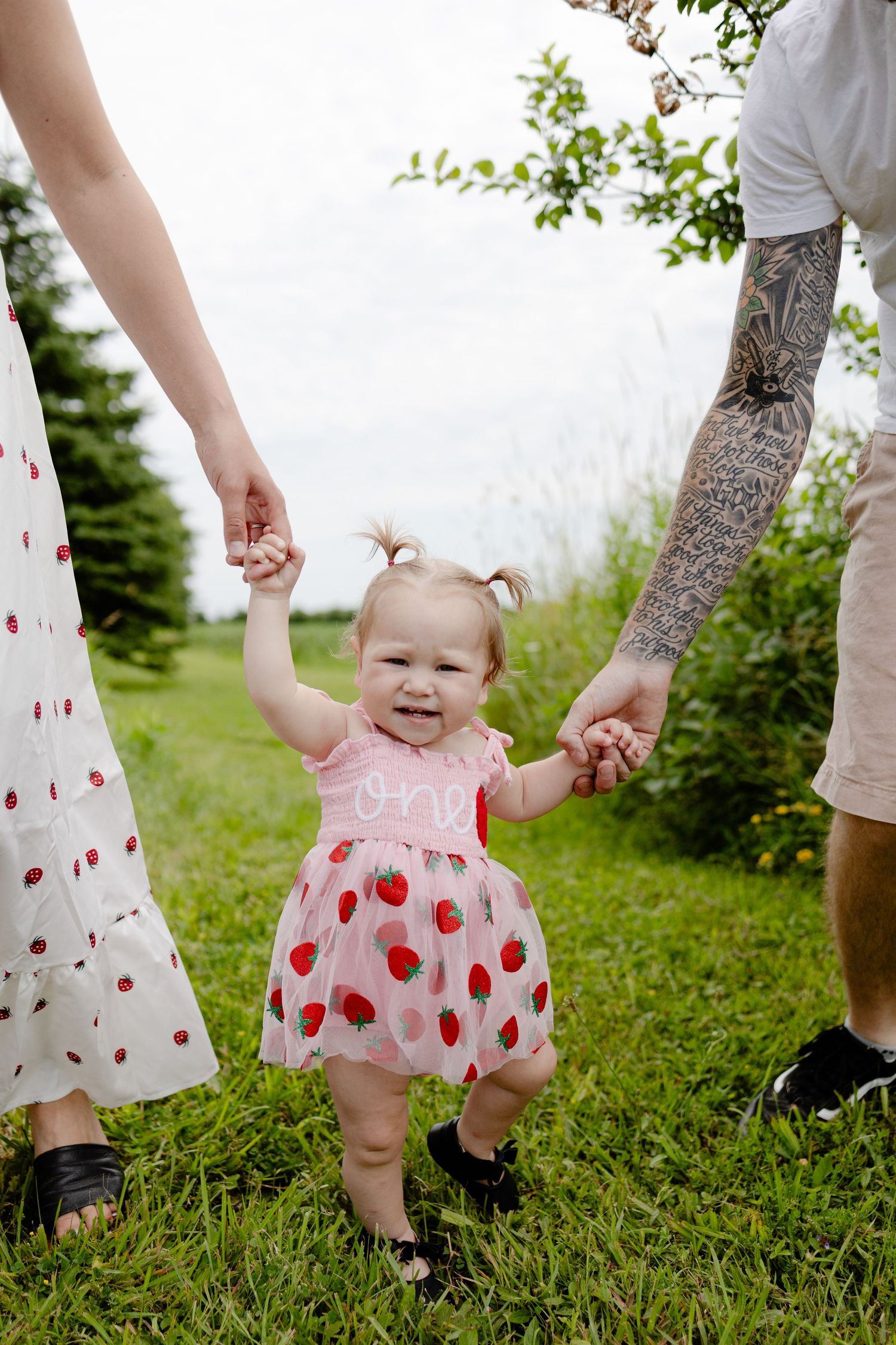 a one year old holding their parents hands during an outdoor photo session